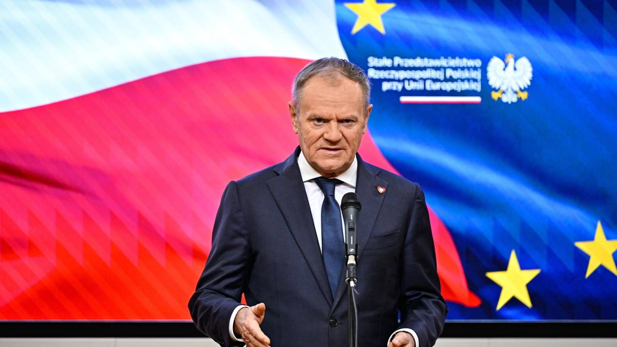 Donald Tusk przemawia przed polską i unijną flagą.