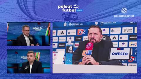 Trzy ekrany telewizyjne. Gł&oacute;wny ekran przedstawia mężczyznę w garniturze siedzącego przy stole i m&oacute;wiącego do mikrofonu, na tle ściany z logo sponsor&oacute;w. Dwa mniejsze ekrany po lewej stronie pokazują dw&oacute;ch innych mężczyzn.