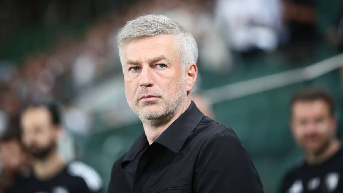 Portret trenera Legii Warszawa, starszego mężczyzny z siwymi włosami, ubrany w czarną koszulę.