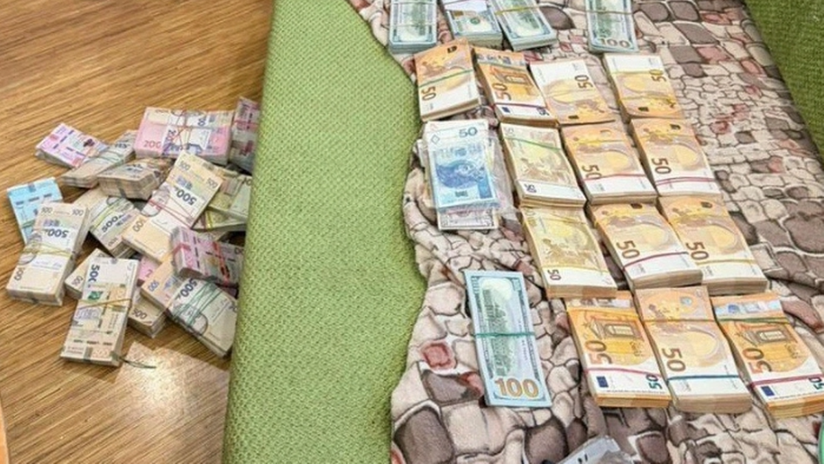 Stosy banknot&oacute;w w r&oacute;żnych walutach, w tym hrywny, euro i dolary, ułożone na podłodze i na tkaninie.