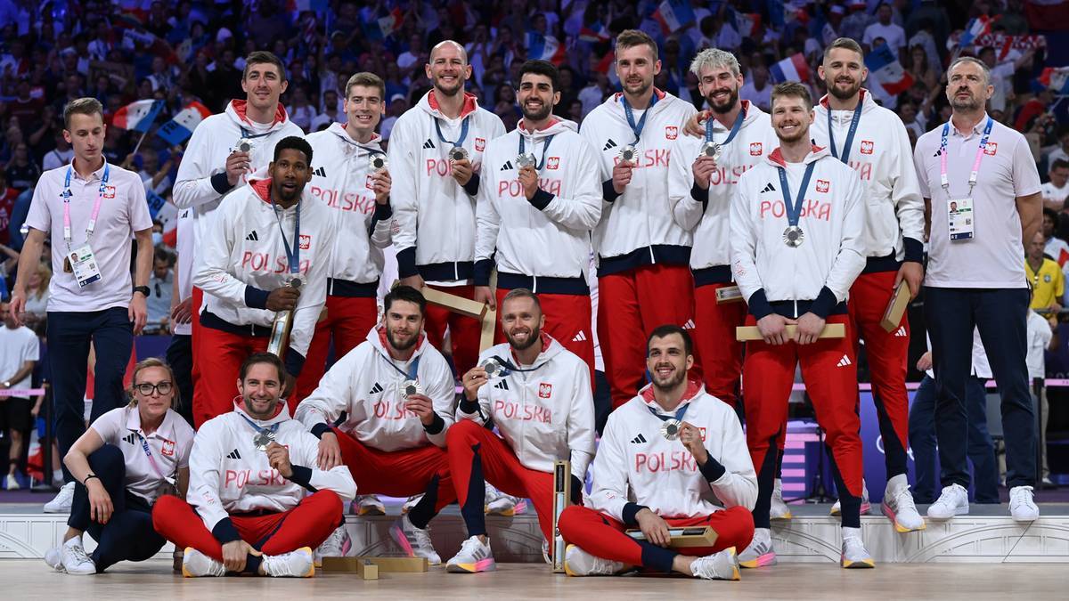 Drużyna polskich siatkarzy w strojach sportowych, z medalami na szyjach, pozująca do zdjęcia.