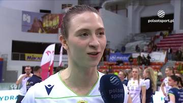 Zbliżenie na twarz siatkarki podczas wywiadu w hali sportowej. W tle widać innych zawodnik&oacute;w i trybuny.