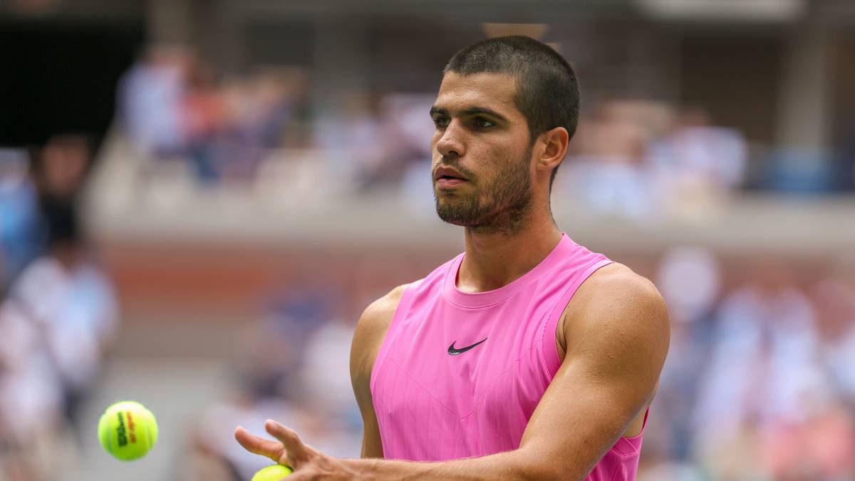 Carlos Alcaraz, tenisista, w różowej koszulce bez rękawów, trzyma piłkę tenisową w dłoni, przygotowuje się do serwisu na tle trybun z widzami.