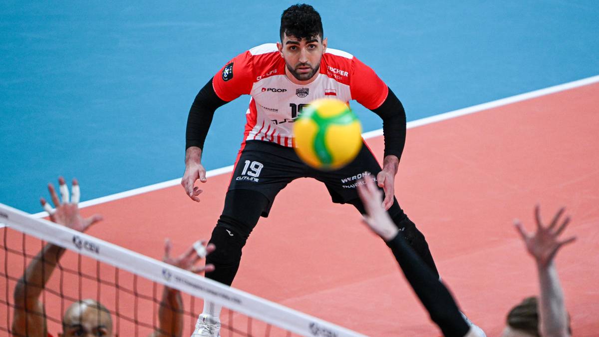 Siatkarz w czerwonej koszulce z numerem 19 podaje piłkę do zagrywki podczas meczu siatkówki.