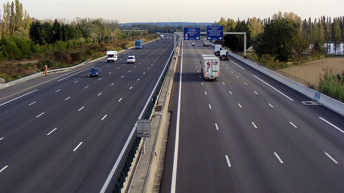 Pusta autostrada z samochodami w oddali, otoczona drzewami i zielenią.