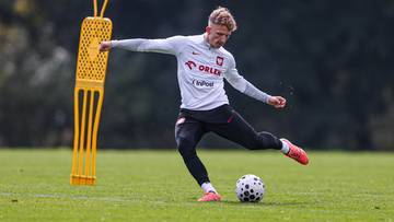 Piłkarz w stroju reprezentacji Polski trenuje kopnięcie piłki na boisku, obok stoi ż&oacute;łty manekin treningowy.