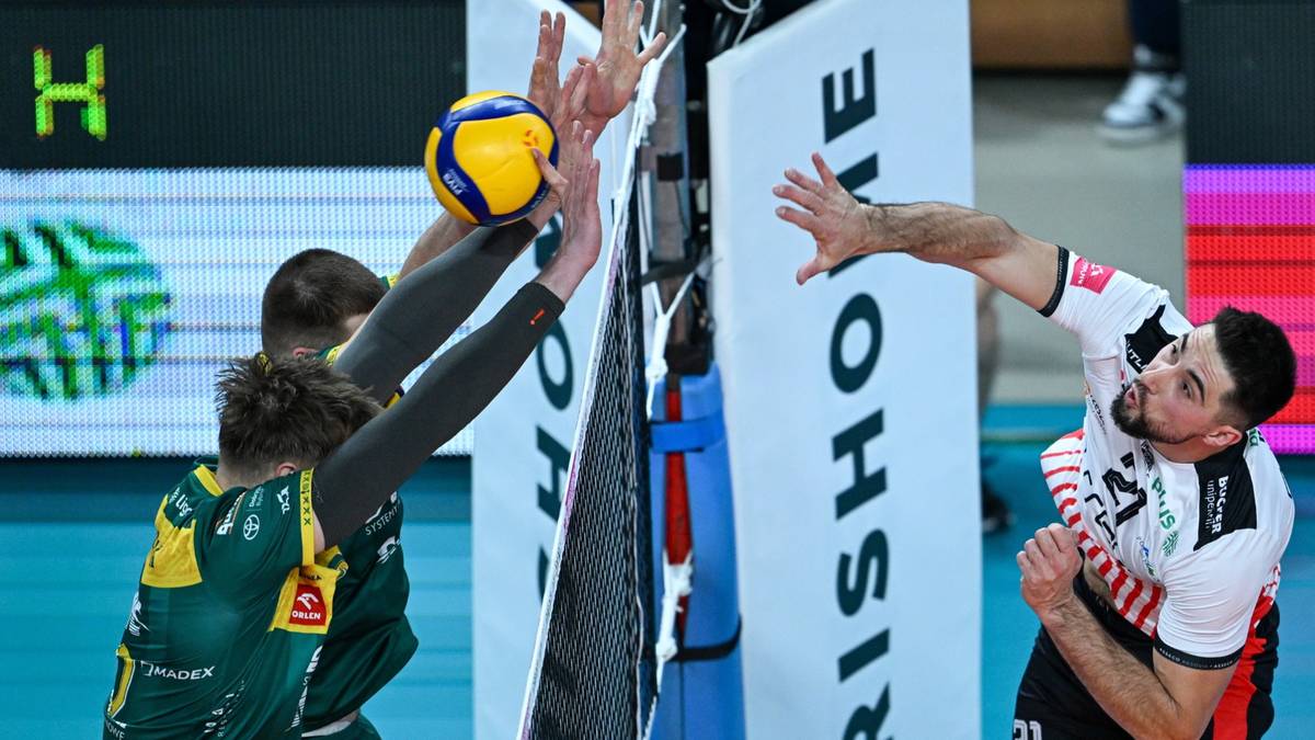 Siatkarz w białej koszulce próbuje zablokować atak przeciwnika.