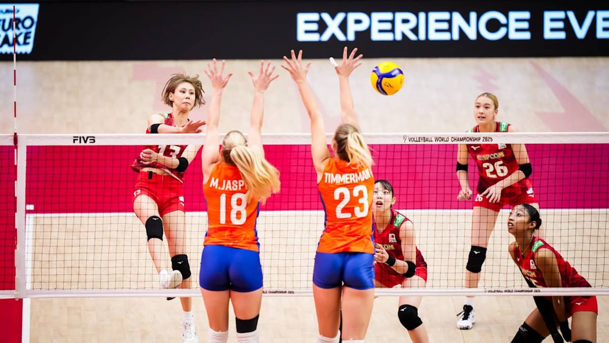 Dwie zawodniczki w strojach sportowych z numerami 18 i 23 blokują piłkę po stronie siatkówki. W tle widoczne są inne zawodniczki oraz siatka. Z góry ekranu wystaje fragment tablicy z napisem "EXPERIENCE EVE".