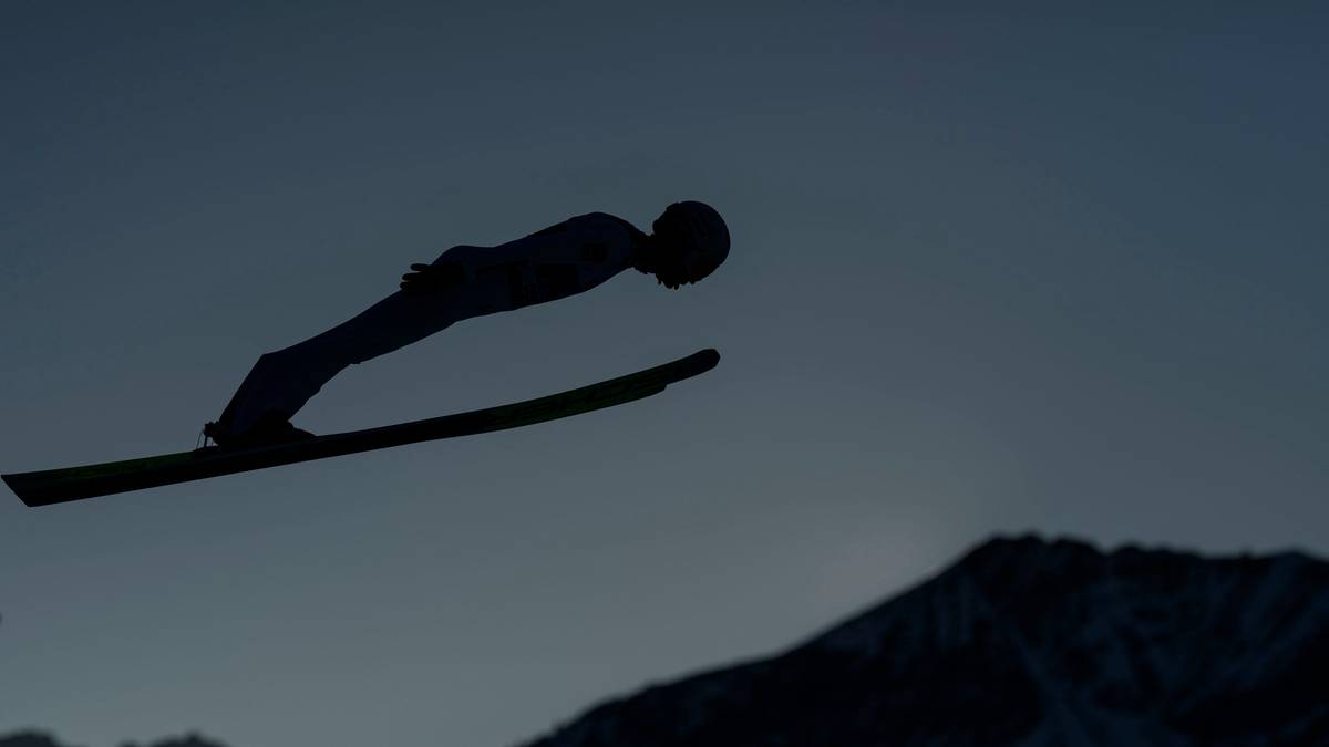Sylwetka skoczka narciarskiego w locie na tle nocnego nieba.