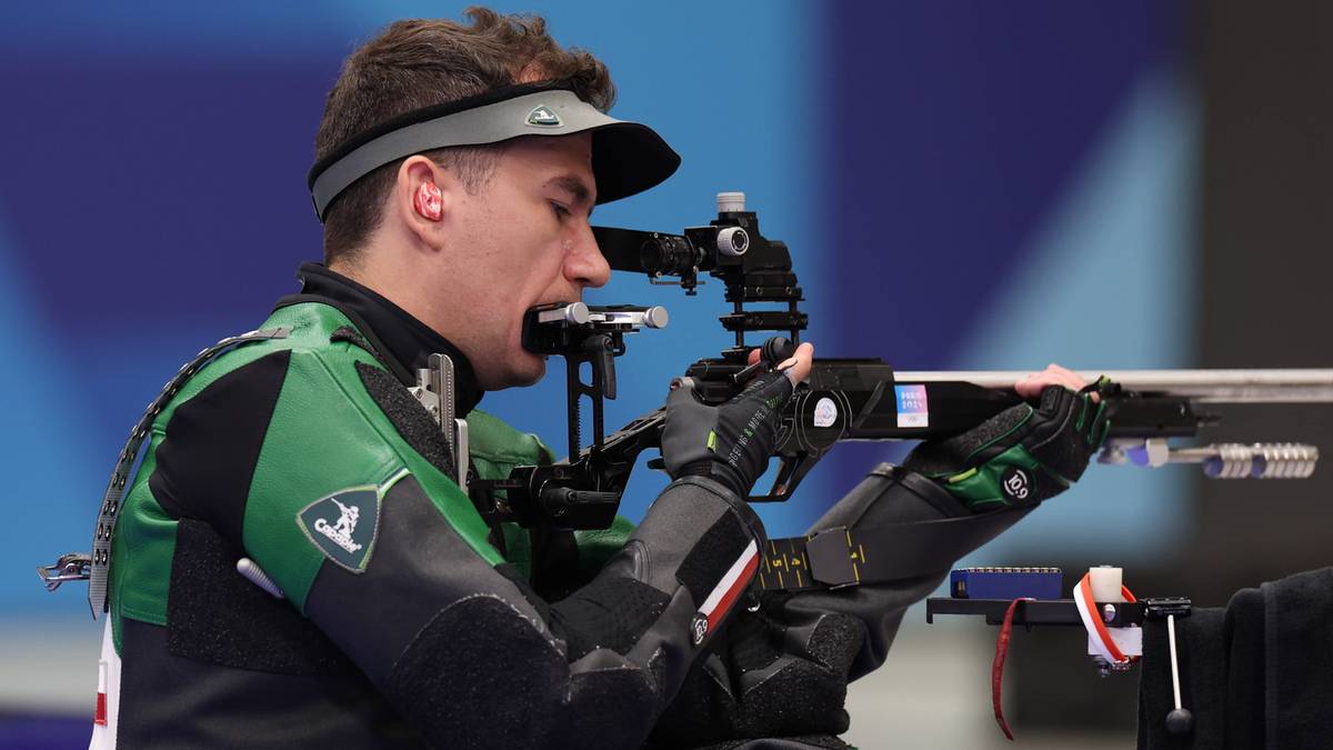 Tomasz Bartnik w pozycji klęczącej oddaje strzał z karabinu sportowego.