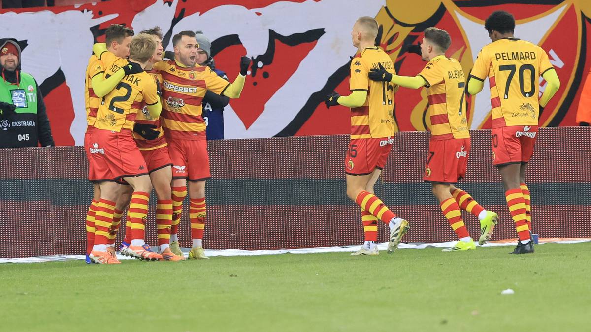 Piłkarze Jagiellonii Białystok w ż&oacute;łto-czerwonych strojach świętują razem na boisku.