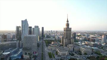 Panorama miasta z Pałacem Kultury i Nauki w centrum, otoczonym przez wsp&oacute;łczesne wieżowce i szeroką ulicę.