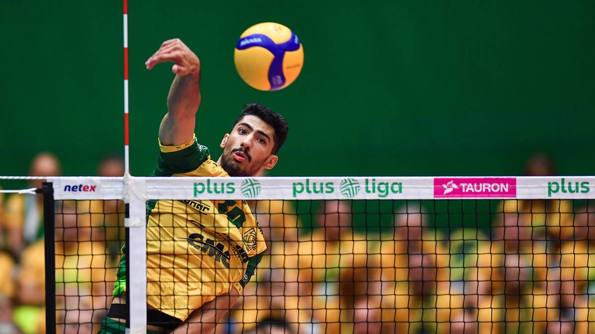 Mężczyzna w żółto-zielonej koszulce siatkarskiej podaje piłkę do siatkówki podczas meczu.