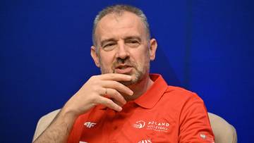 Mężczyzna w czerwonej koszulce z logo siatkówki, opiera dłoń na brodzie.