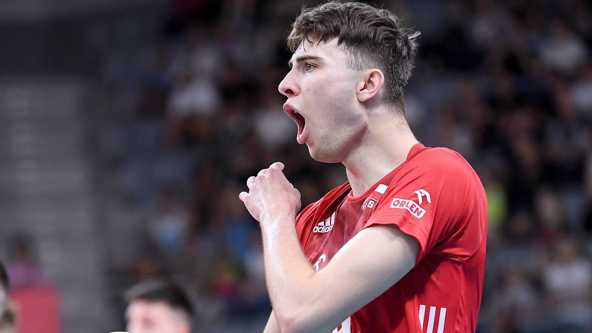 Siatkarz w czerwonej koszulce z numerem 13 trzyma piłkę siatkową i krzyczy z radości, obok stoi inny zawodnik