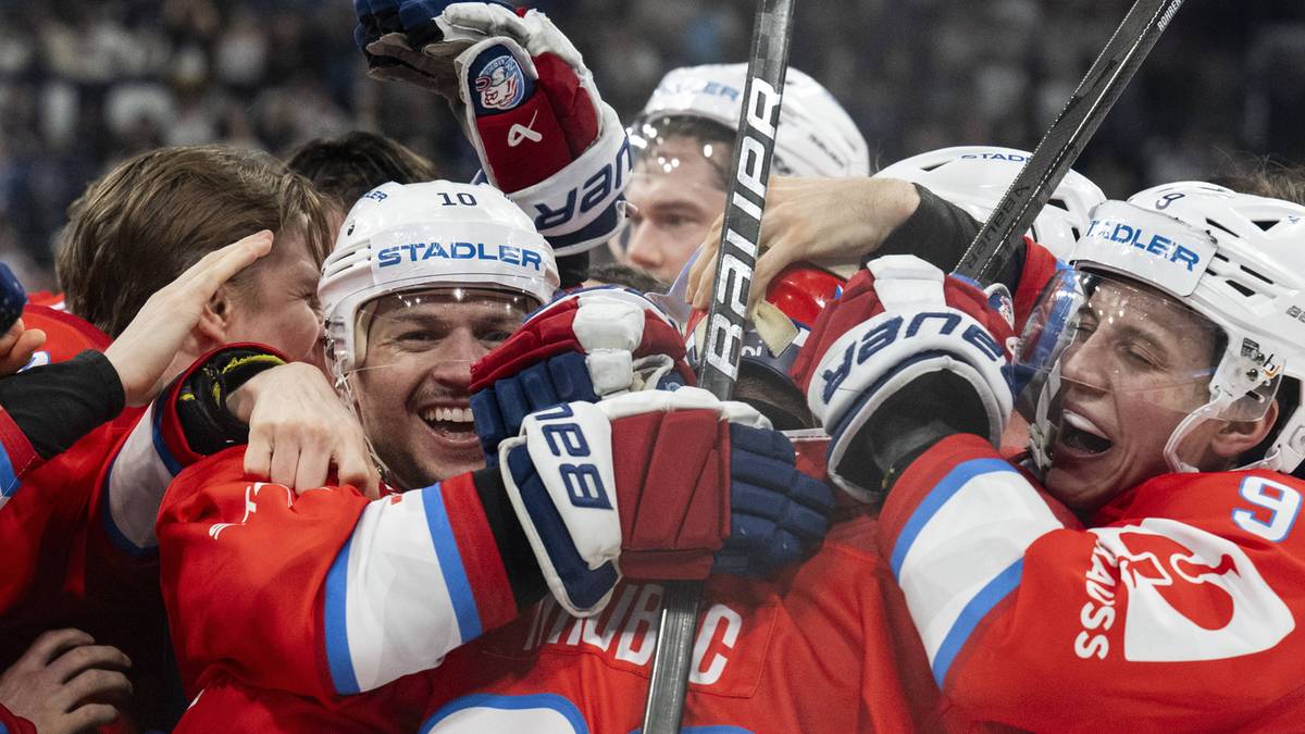 Hokeiści w czerwonych strojach świętujący razem z uniesionymi kijami hokejowymi.