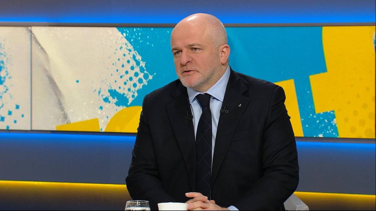 Mężczyzna w garniturze i krawacie siedzi przy stole i mówi