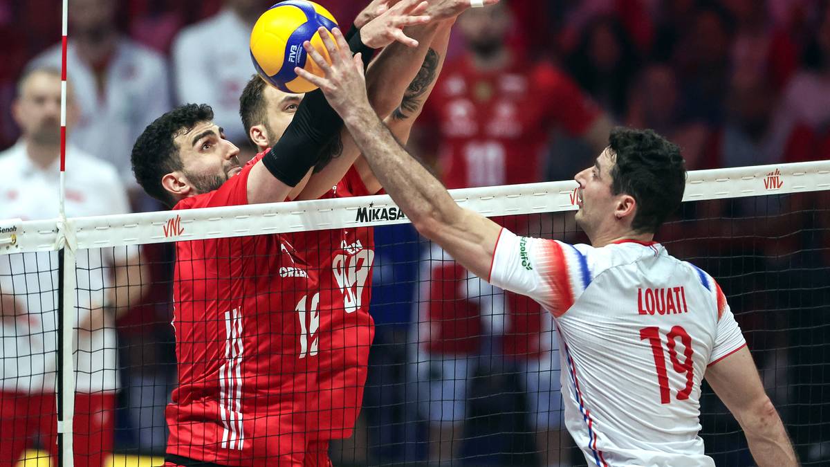 Siatkarze walczą o piłkę przy siatce podczas meczu.