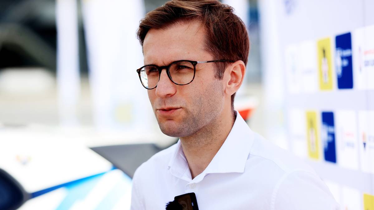 Mężczyzna w białej koszuli i okularach z ciemnymi oprawkami patrzy przed siebie z lekko zmarszczonymi brwiami.