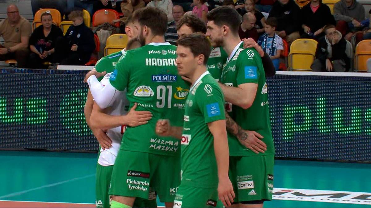 Drużyna siatkarzy w zielonych strojach świętuje zwycięstwo, z zawodnikami przytulającymi się na boisku.