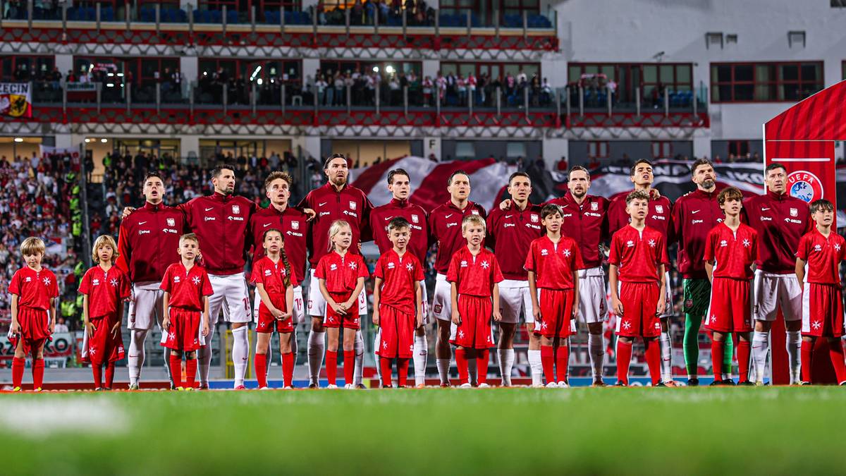 Reprezentacja Polski w piłce nożnej w czerwonych strojach, stojąca w rzędzie na boisku.