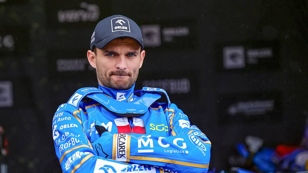 Żużlowiec w niebieskim kombinezonie i czapce z daszkiem z logo PGE Ekstraliga.