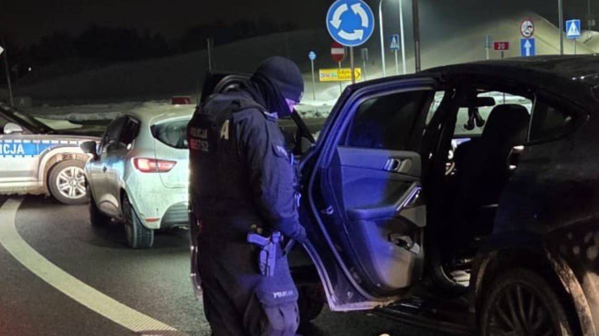 Policjant w pełnym umundurowaniu przy otwartych drzwiach samochodu.