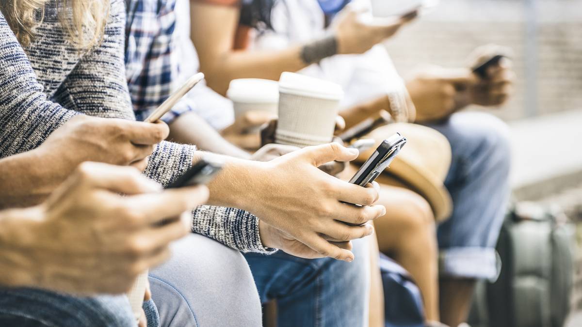 Grupa os&oacute;b siedzących obok siebie, każda skupiona na ekranie swojego smartfona.