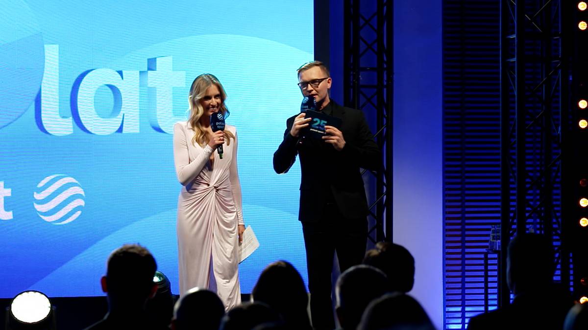 Kobieta i mężczyzna stoją na scenie, prowadząc wydarzenie z mikrofonami.