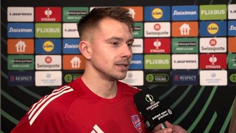 Fran Tudor, piłkarz w czerwonej koszulce, udziela wywiadu przed ścianą z logotypami sponsor&oacute;w.