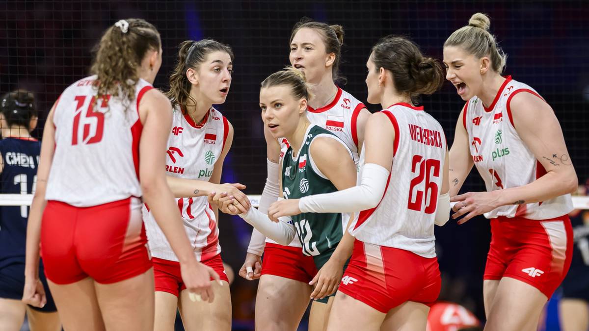 Siatkarki w białych i czerwonych strojach sportowych świętują razem z jedną zawodniczką w zielonym stroju po meczu.