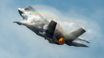 Myśliwiec F-15 leci na tle nieba, tworząc smugę pary wodnej przypominającą tęczę.