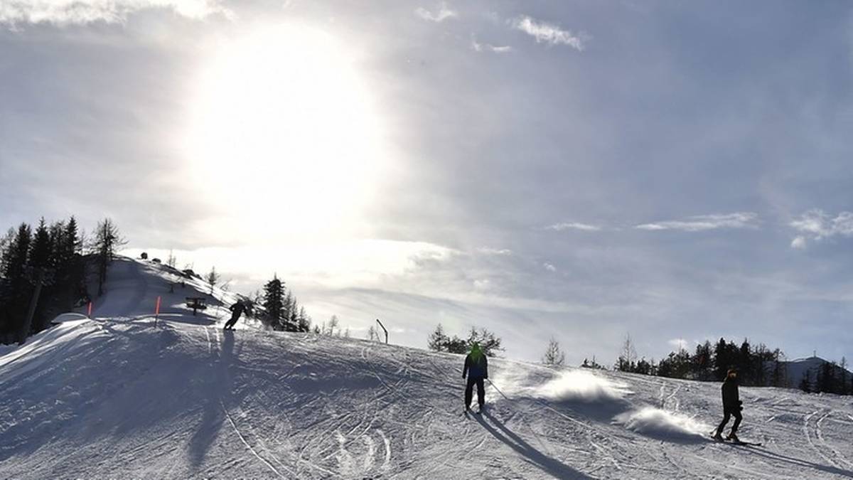 Osoby jeżdżące na nartach po ośnieżonym stoku w słoneczny dzień.