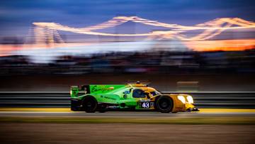 Samochód wyścigowy z numerem 43 na torze w kolorach zielonym i żółtym, z rozmazanymi światłami w tle.