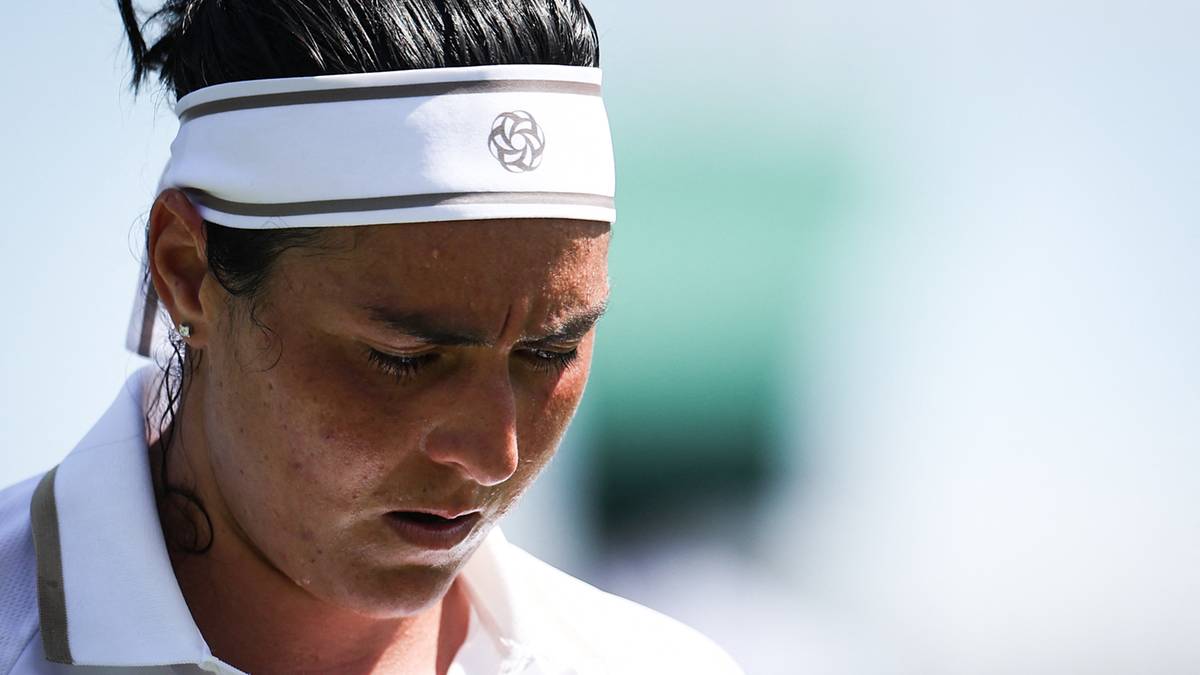 Ons Jabeur, tunezyjska tenisistka, z opaską na głowie, w trakcie meczu, z wyrazem zmęczenia na twarzy.