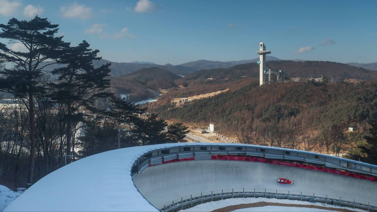 Tor bobslejowy w zimowej scenerii, z widocznym zjazdem i zakrętem, na tle górzystego krajobrazu i wieży.