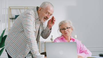 Starsza para patrząca na laptopa, mężczyzna wskazuje coś na ekranie, a kobieta słucha go z uwagą.