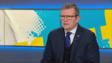 Mężczyzna w okularach i garniturze, w ciemnej marynarce i kamizelce, m&oacute;wi do kamery.