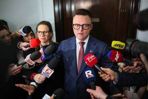Szymon Hołownia otoczony przez dziennikarzy z mikrofonami podczas wypowiedzi w Sejmie.
