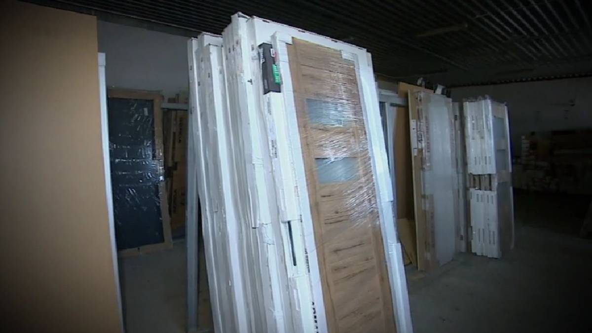 Stos nowych drzwi wewnętrznych, owiniętych folią ochronną, ustawionych pionowo w magazynie.