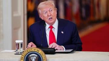 Prezydent USA Donald Trump przemawia przy stole z mikrofonem i pieczęcią prezydencką.