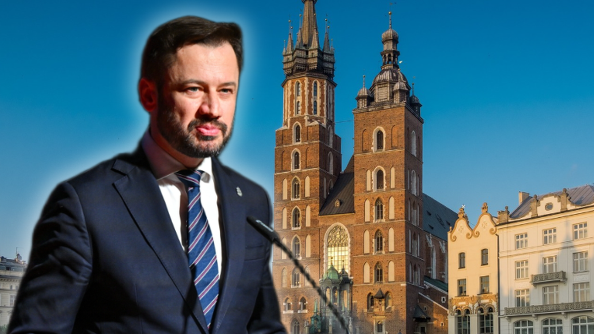 Polityk w garniturze, Marek Sawicki, przemawia przed mikrofonem na tle Kościoła Mariackiego na Rynku Gł&oacute;wnym w Krakowie.