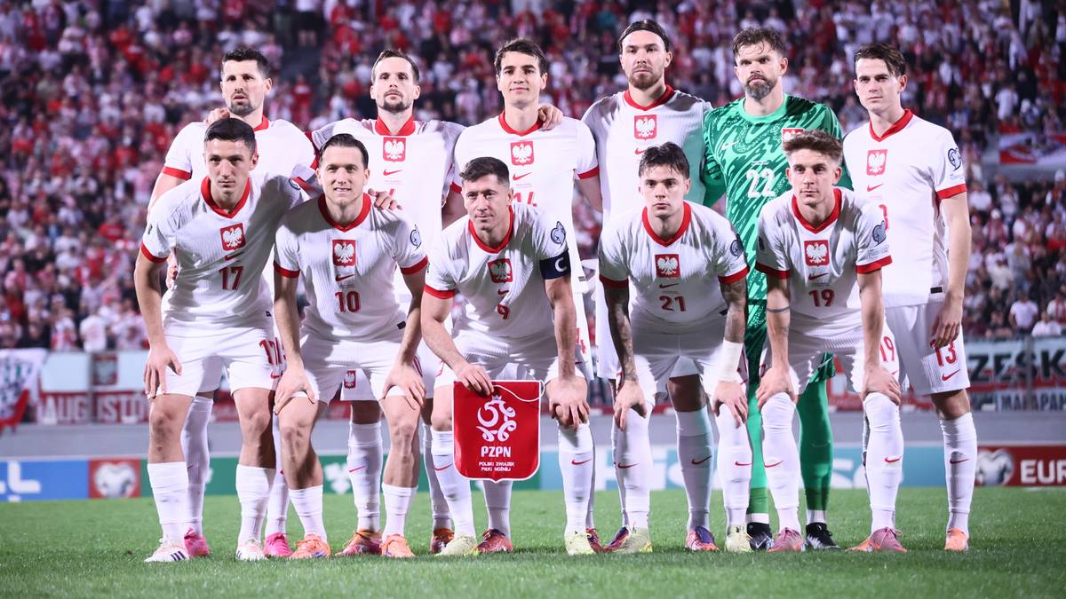Drużyna piłkarska Polski w białych strojach stoi na boisku przed kibicami.