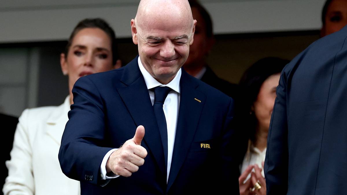 Mężczyzna w granatowym garniturze i białej koszuli z krawatem, pokazuje kciuk w g&oacute;rę i uśmiecha się.