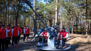 Drużyna rugby w czerwonych kamizelkach zwiedza historyczną artylerię na świeżym powietrzu, z dużą armatą w centrum uwagi.