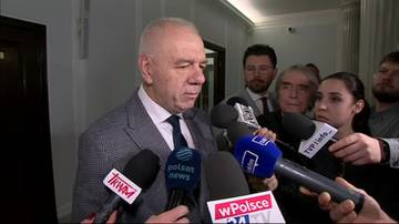 Jacek Sasin w garniturze otoczony przez dziennikarzy z mikrofonami, udziela wywiadu.