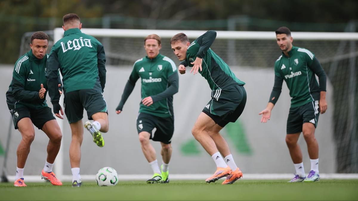 Pięciu piłkarzy w zielonych strojach treningowych Legii Warszawa ćwiczy na boisku piłkarskim, jeden z nich kopie piłkę.