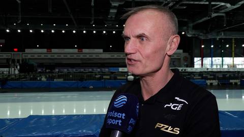 Rafał Ślusarski, ubrany w czarną bluzę z logotypami PGE i PZKS, udziela wywiadu na tle lodowiska.
