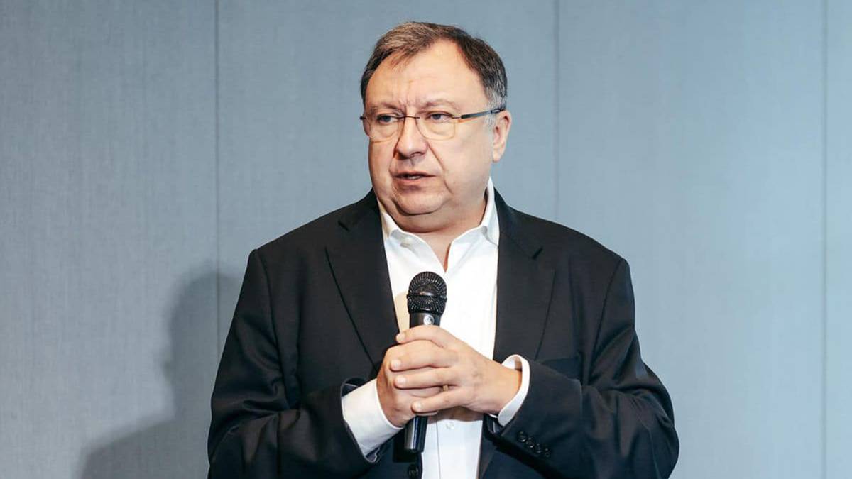 Mężczyzna w garniturze z mikrofonem w dłoni przemawia.