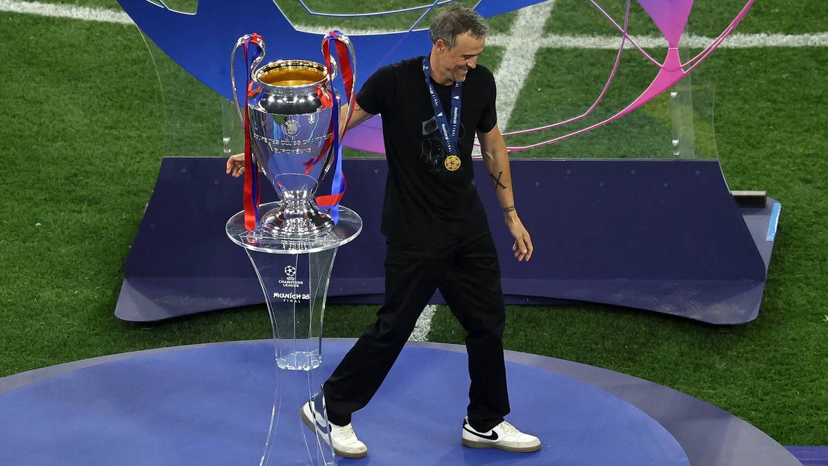 Mężczyzna w czarnym stroju i z medalem na szyi, z dumą niesie Puchar Ligi Mistrzów.